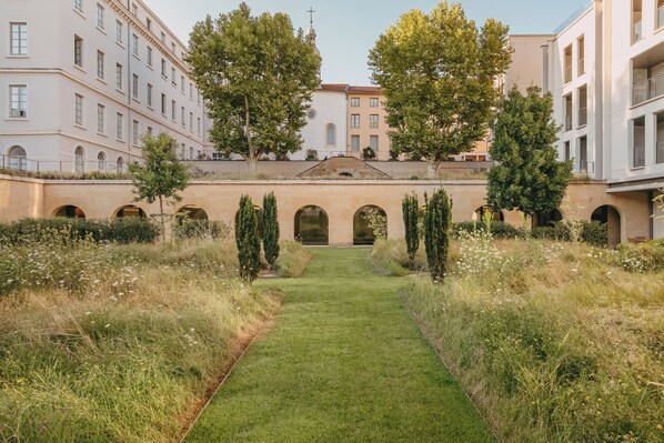 A courtyard with a central pathway, surrounded by buildings with arched windows and a church with a dome. - Villa Maïa (Lyon)
