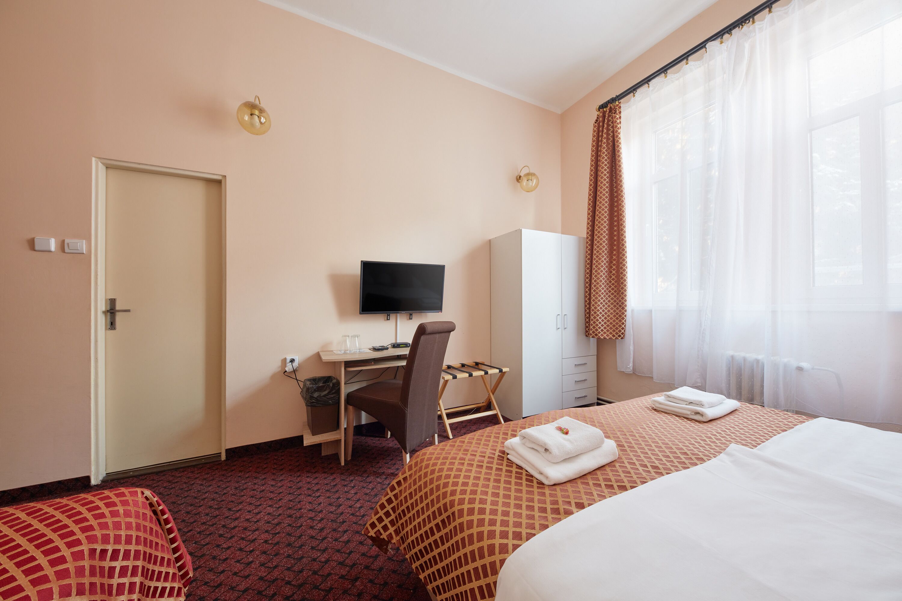 A hotel room with two beds, a desk with a chair, a television, and a wardrobe.