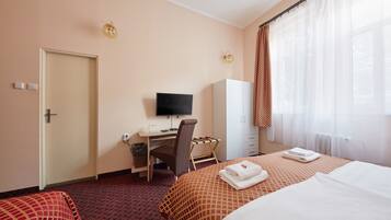 A hotel room with two beds, a desk with a chair, a television, and a wardrobe.