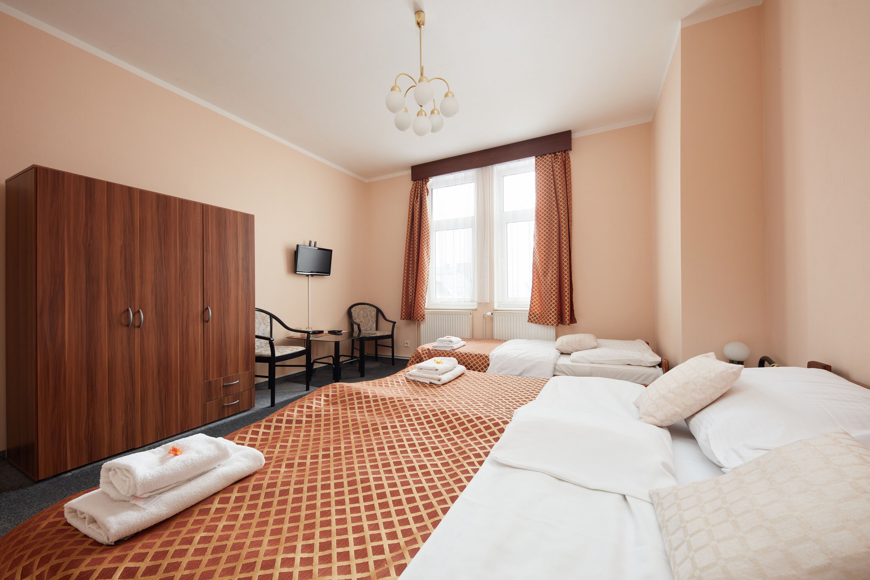 Una habitación de hotel con una cama grande, un armario, un escritorio con silla, un televisor y una ventana con cortinas.