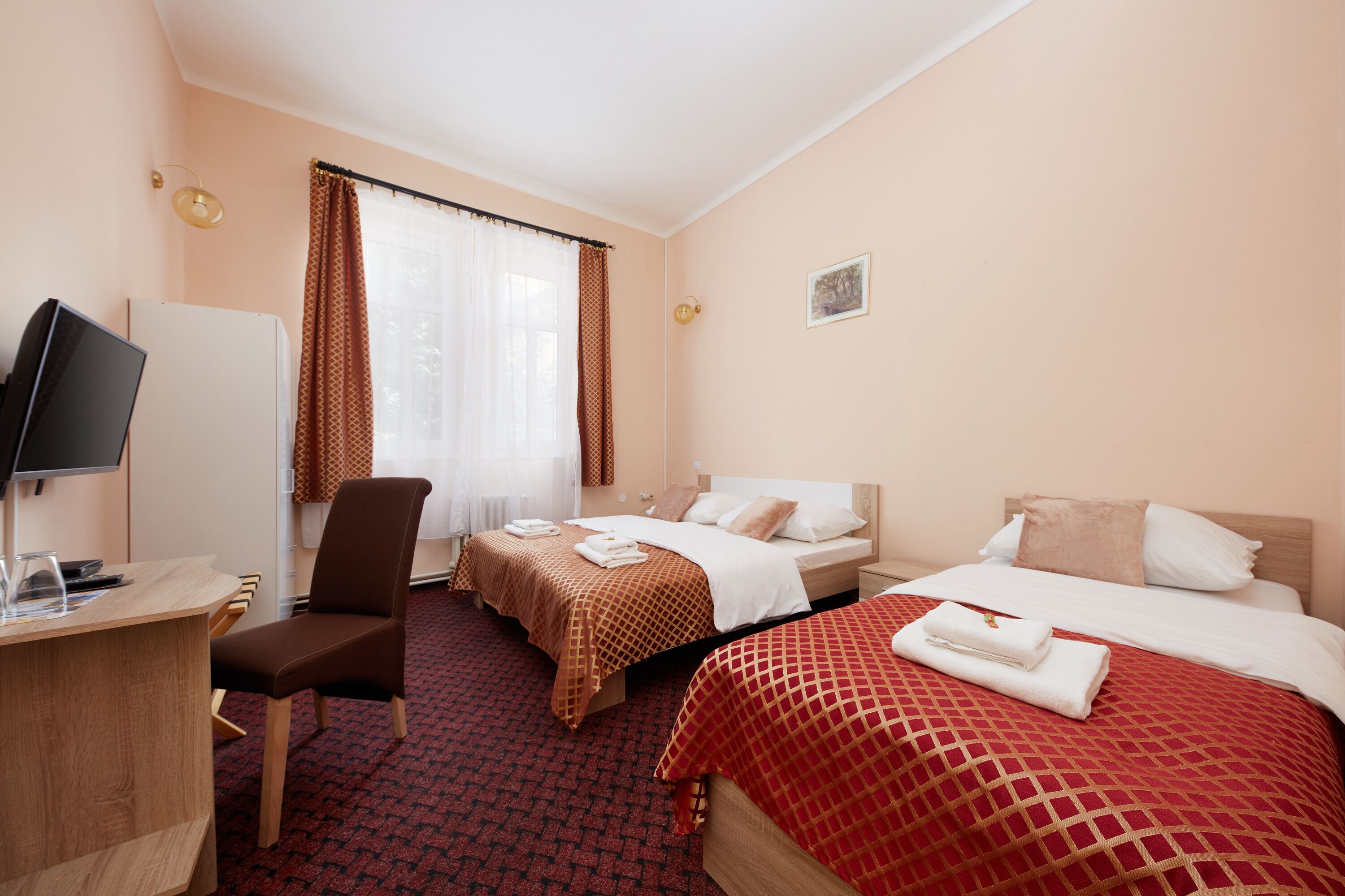 A hotel room with two beds, a desk, a chair, and a television.