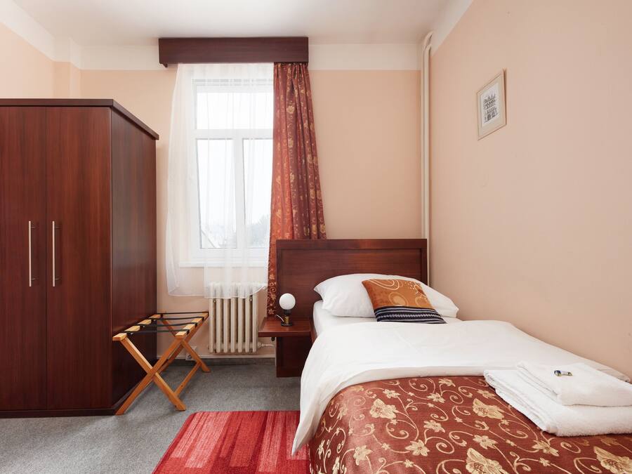 A hotel room with a bed, a wardrobe, a radiator, and a window with curtains.