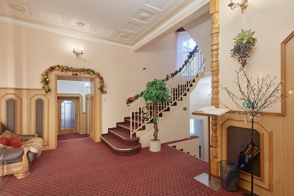 A grand staircase with a red carpet, a wooden bench, and a fireplace with a decorative plant.