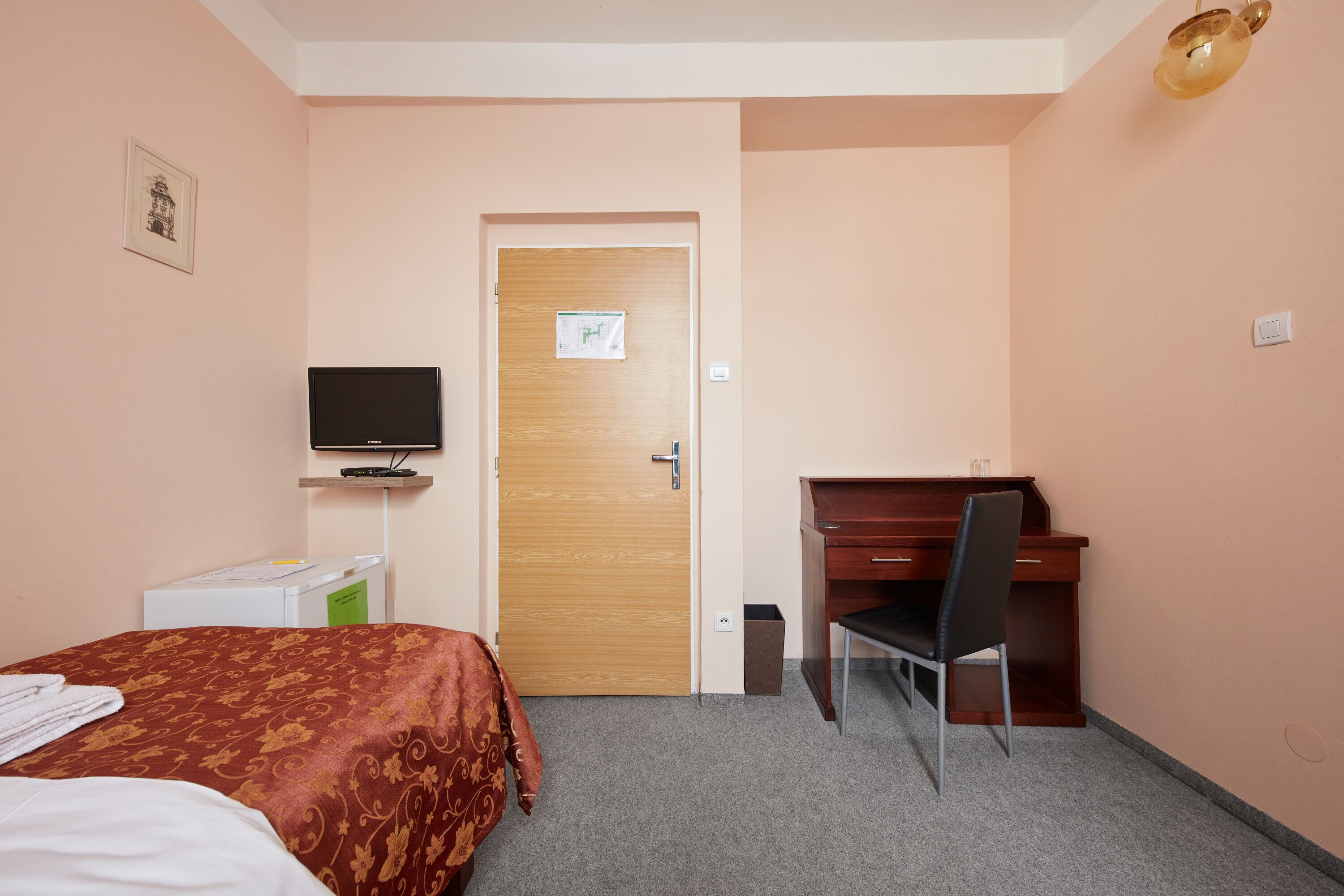 Habitación de hotel con cama, escritorio, silla, televisor y puerta con un cartel.