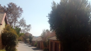 A paved pathway leading to a row of brick buildings with a clear sky above. - The Royal Princess Garden - Honeydew (Roodepoort)