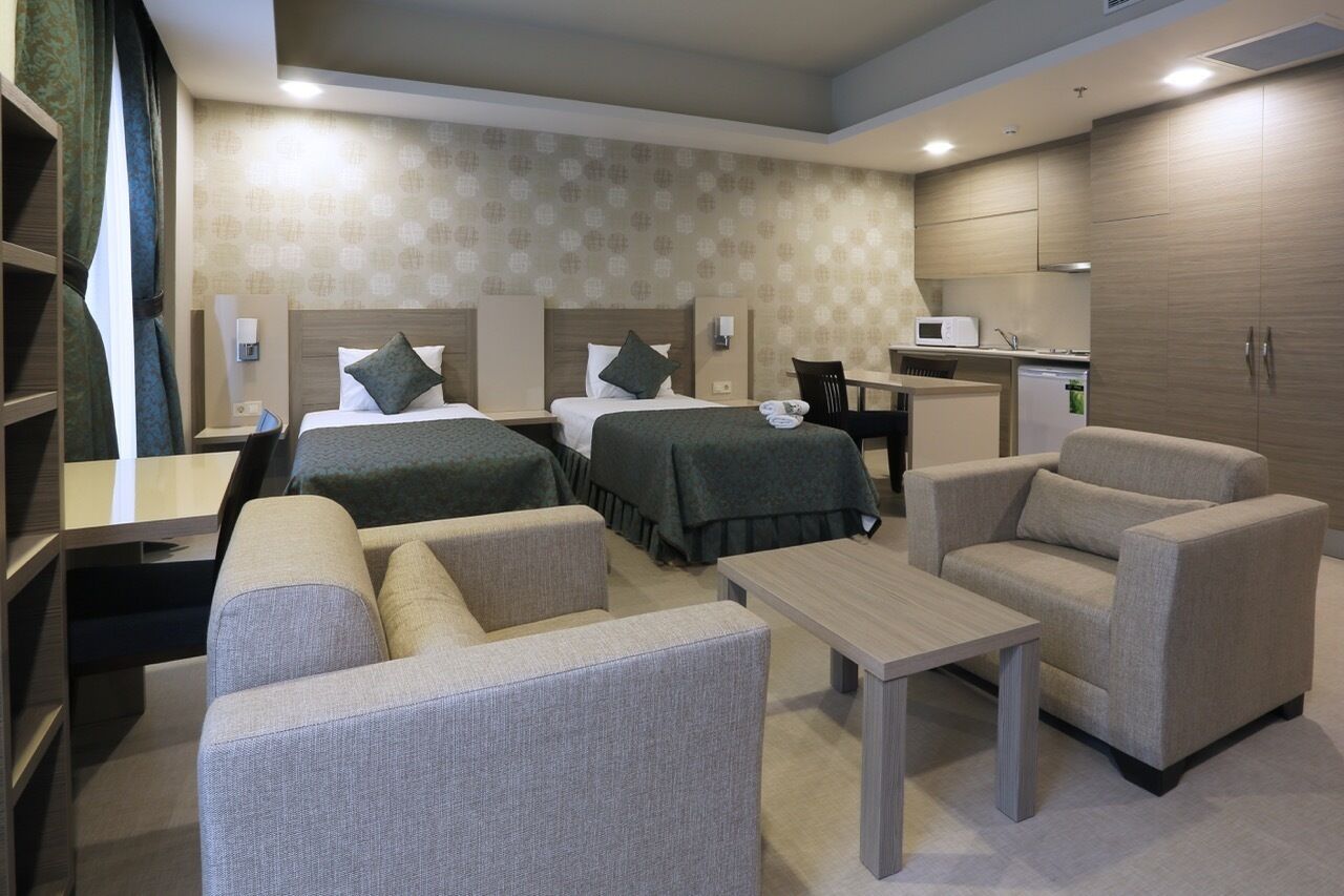 Habitación de hotel con dos camas, un escritorio, una silla, un sofá y una kitchenette.