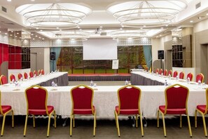 A conference room with a long table, red chairs, and a stage with a screen. - Sakarya Sen Hotel (Serdivan)