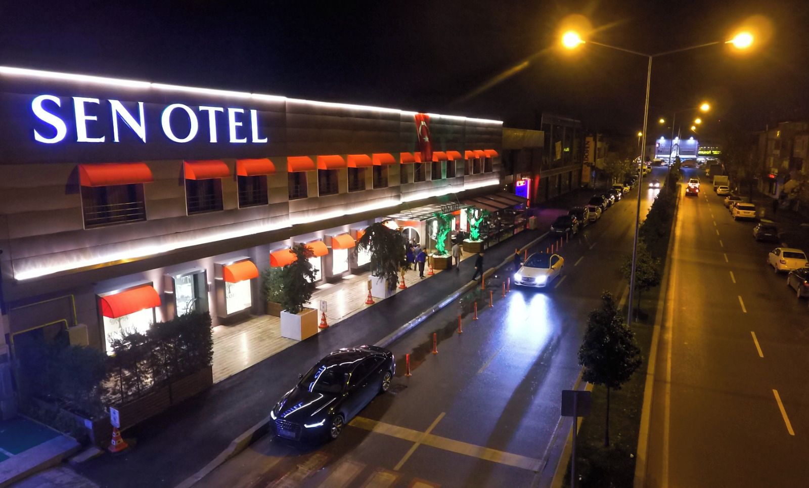 A hotel named SEN OTEL with a modern facade, outdoor seating area, and a well-lit entrance.