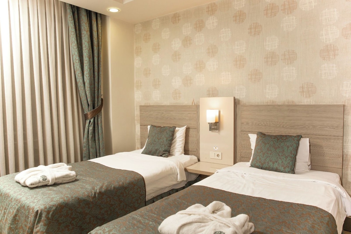 A hotel room with two beds, each with a headboard, a bedside table, and a wall-mounted light.