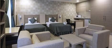 Ein Hotelzimmer mit zwei Betten, einem Schreibtisch, einem Stuhl, einem kleinen Tisch und einer Küchenzeile.