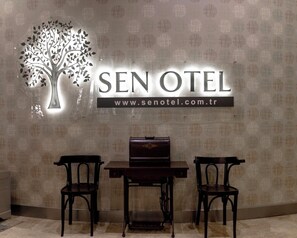 A hotel reception area with a sign reading 'SEN OTEL' and a website address. There is a table with two chairs in front of the sign. - Sakarya Sen Hotel (Serdivan)