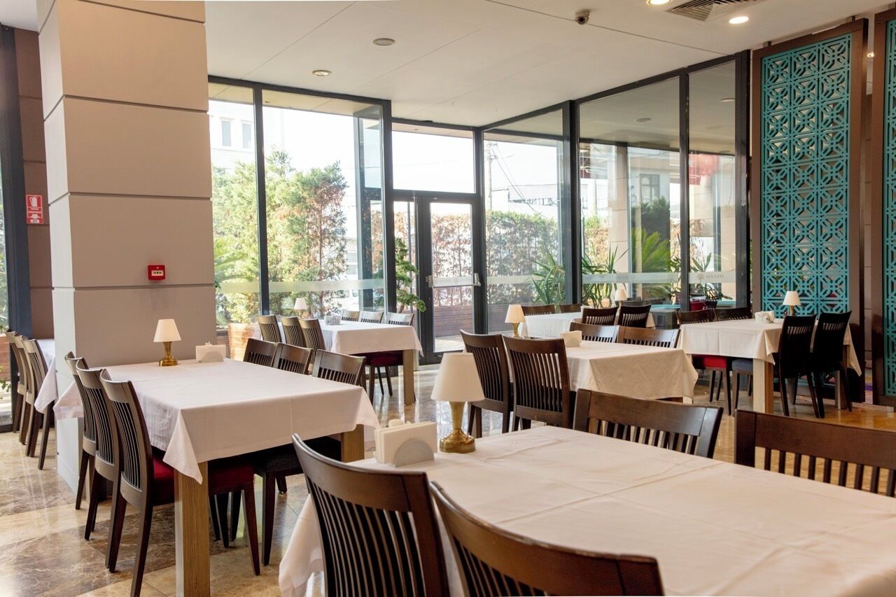Un restaurante con varias mesas y sillas, amplias ventanas y una pared decorativa.