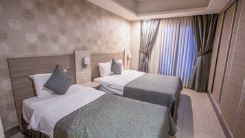 A hotel room with two beds, a large window with curtains, and a patterned wallpaper.