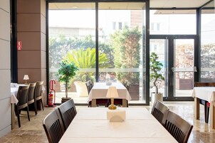 Un comedor con mesas y sillas, un extintor y vista al exterior.