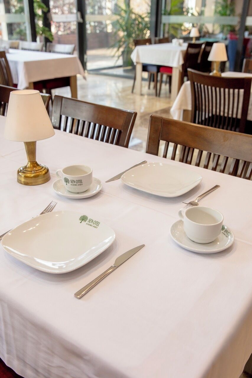 Una mesa de comedor dispuesta con platos, tazas, cubiertos y una lámpara.