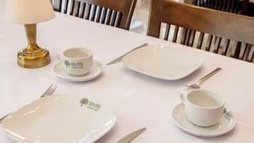 Una mesa de comedor dispuesta con platos, tazas, cubiertos y una lámpara.