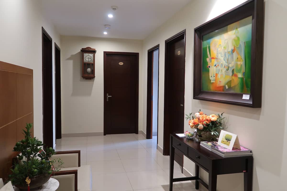 A hallway with a wooden door, a clock, a framed painting, and a desk with a vase of flowers.