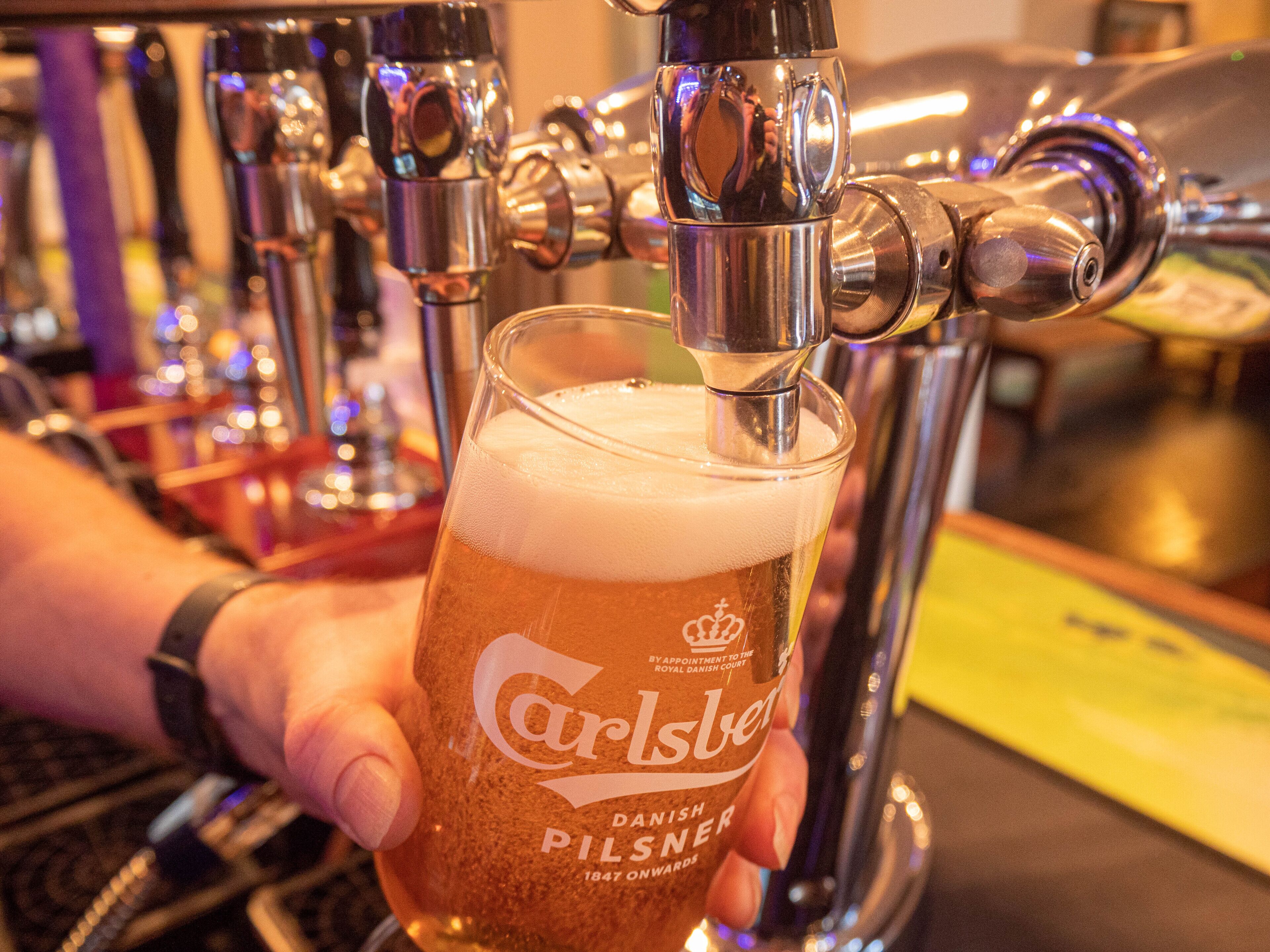A hand holding a glass of Carlsberg Pilsner beer being poured from a tap.