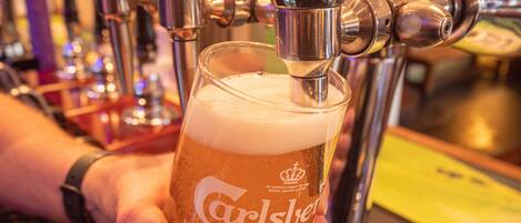 A hand holding a glass of Carlsberg Pilsner beer being poured from a tap.