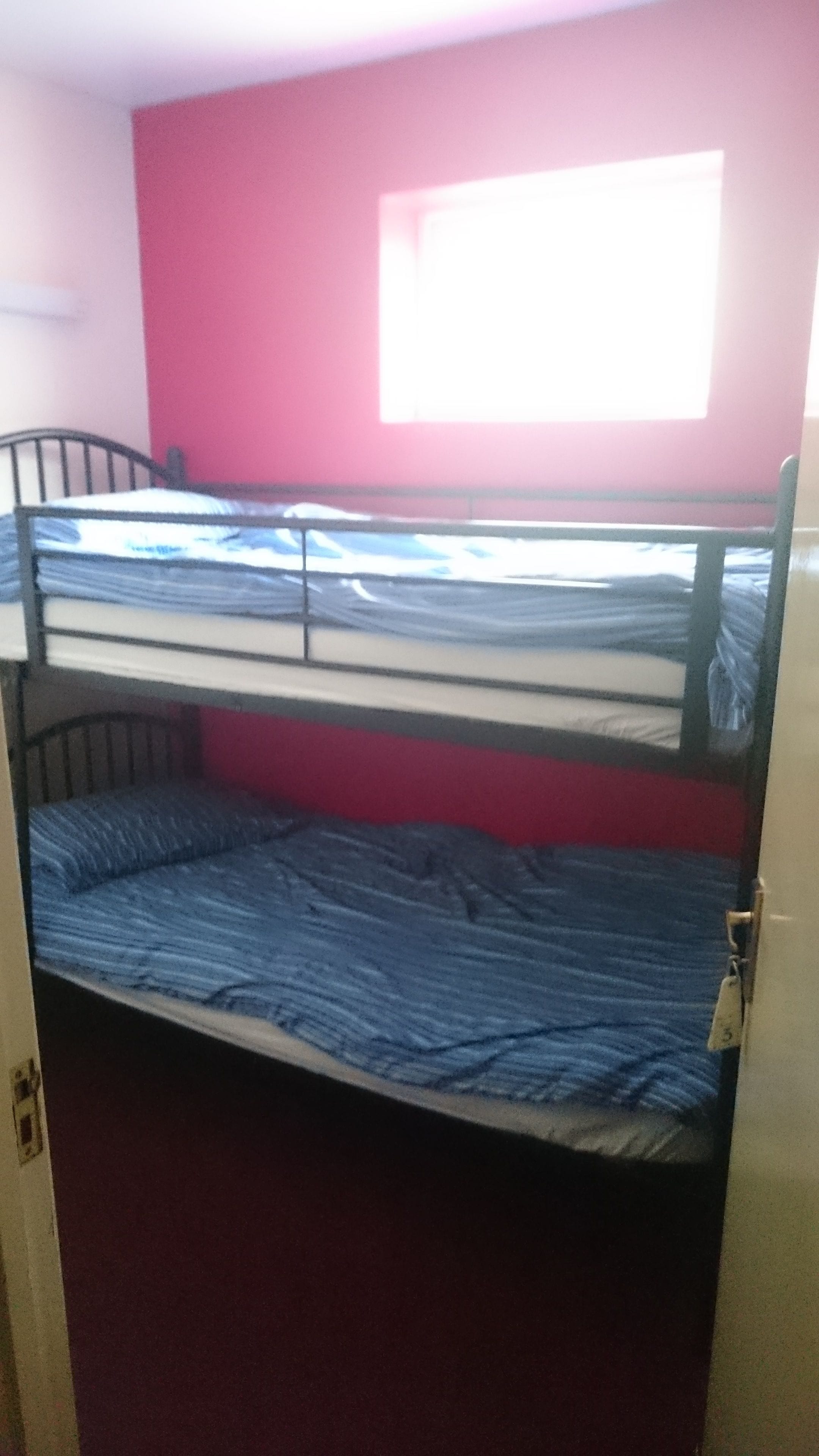 A bunk bed with blue bedding in a room with pink walls and a window.
