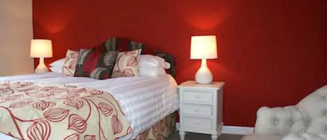 A bedroom with a bed, two bedside tables with lamps, a chair, and a red accent wall.