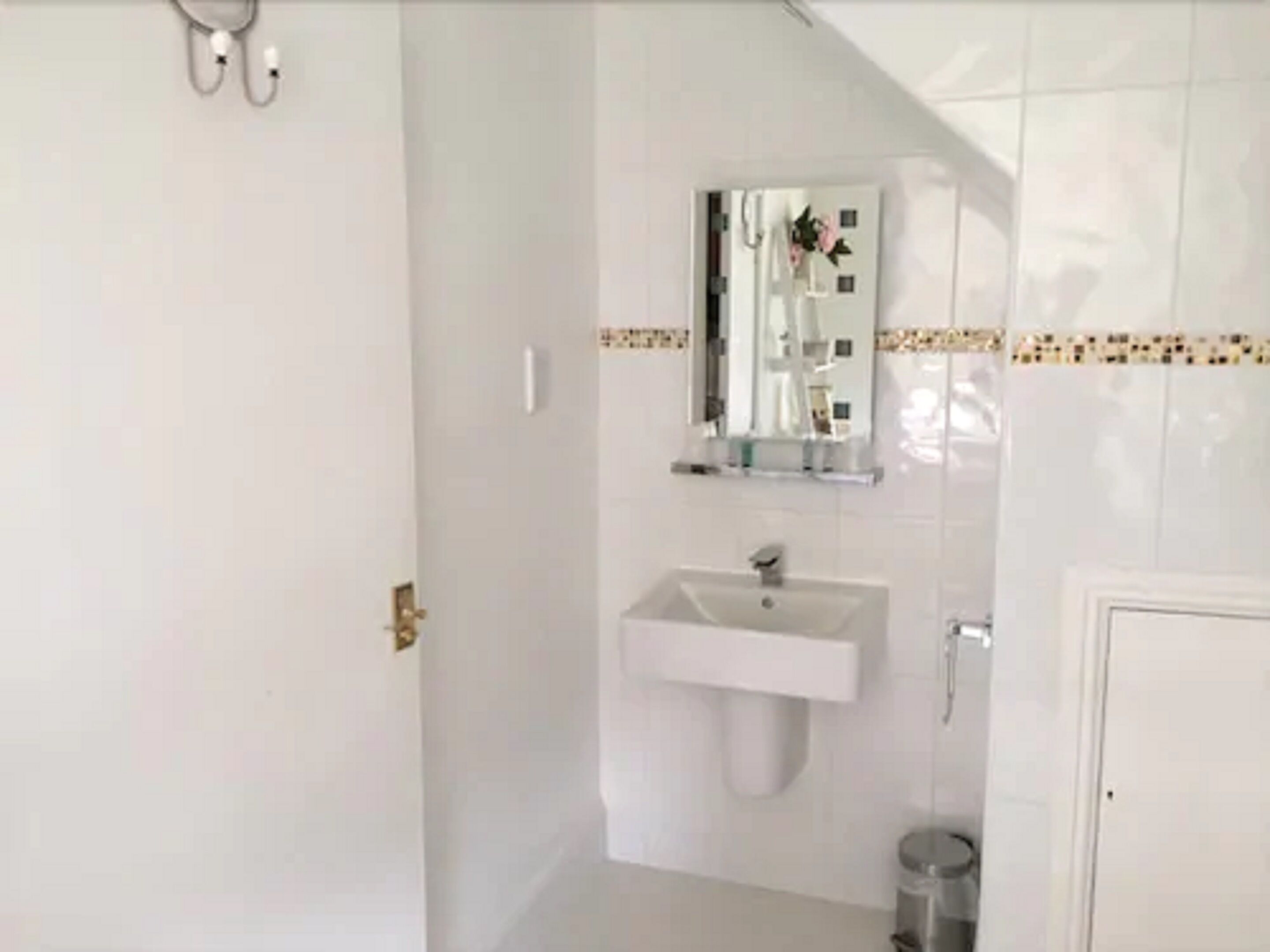 A bathroom with a white sink, a mirror, and a small trash bin.