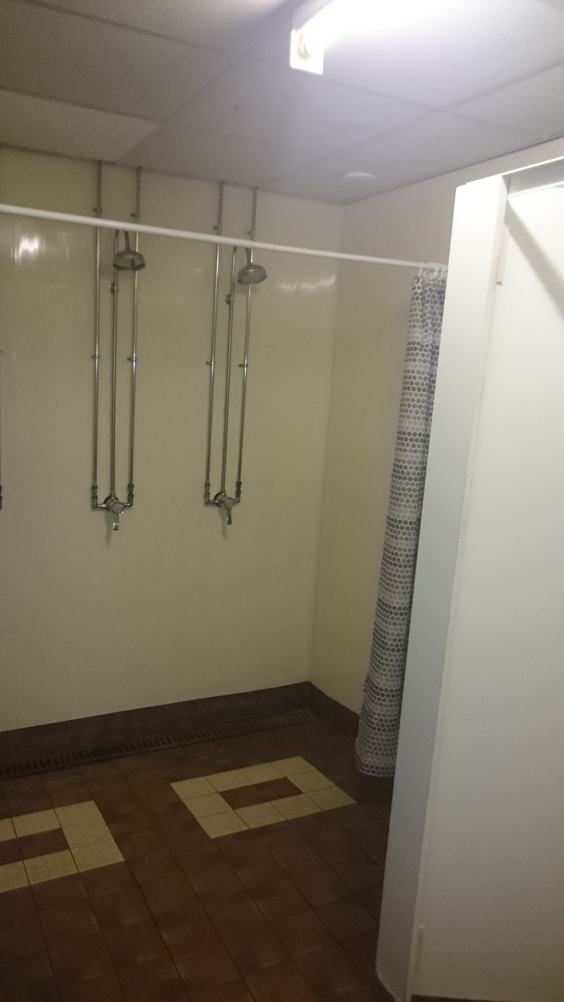 A bathroom with two showerheads, a tiled floor, and a white door.