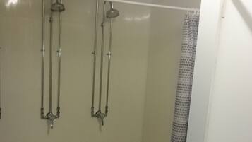 A bathroom with two showerheads, a tiled floor, and a white door.