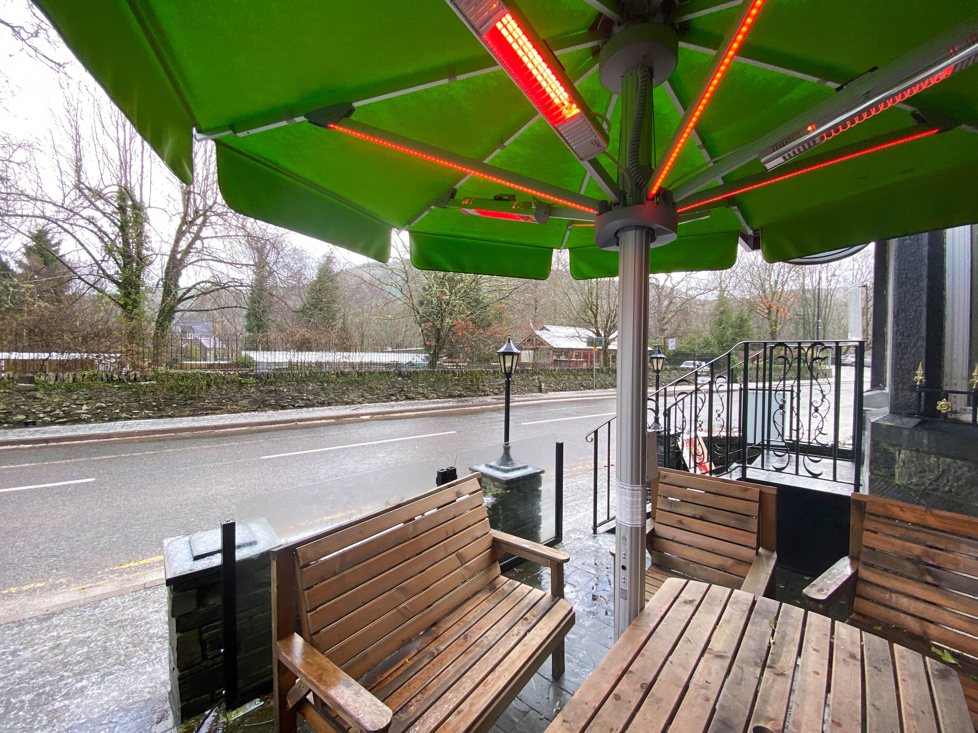 Un espace extérieur aménagé avec des bancs en bois et un parasol vert pour offrir de l’ombre.