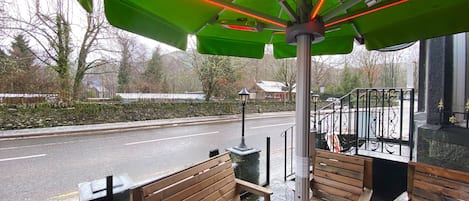 An outdoor seating area with wooden benches and a green umbrella providing shade.