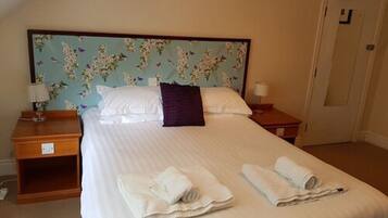 A neatly made bed with white linens, a floral headboard, and two rolled towels on the bed.