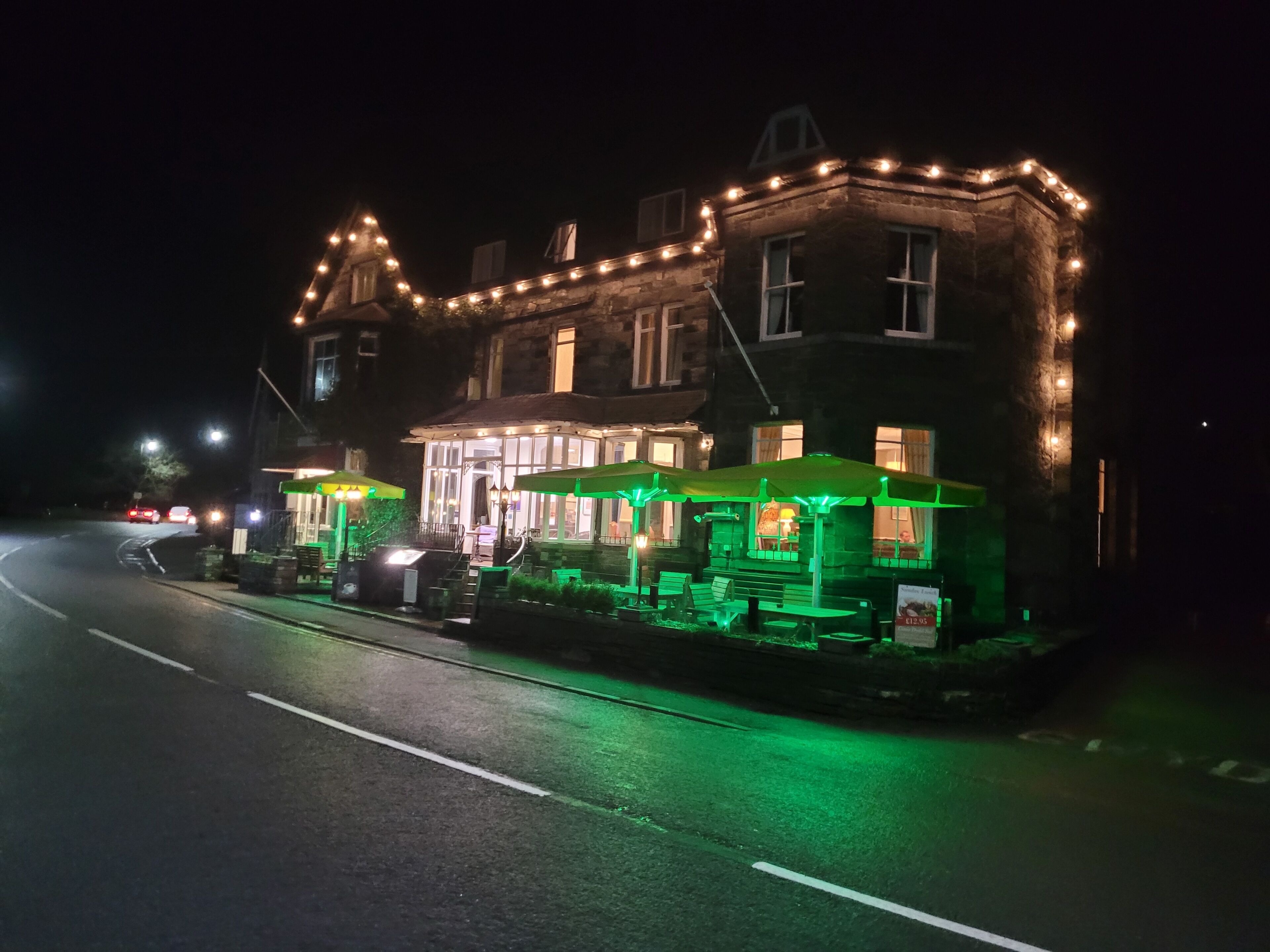 A historic building with a pub on the ground floor, featuring outdoor seating and a well-lit entrance.