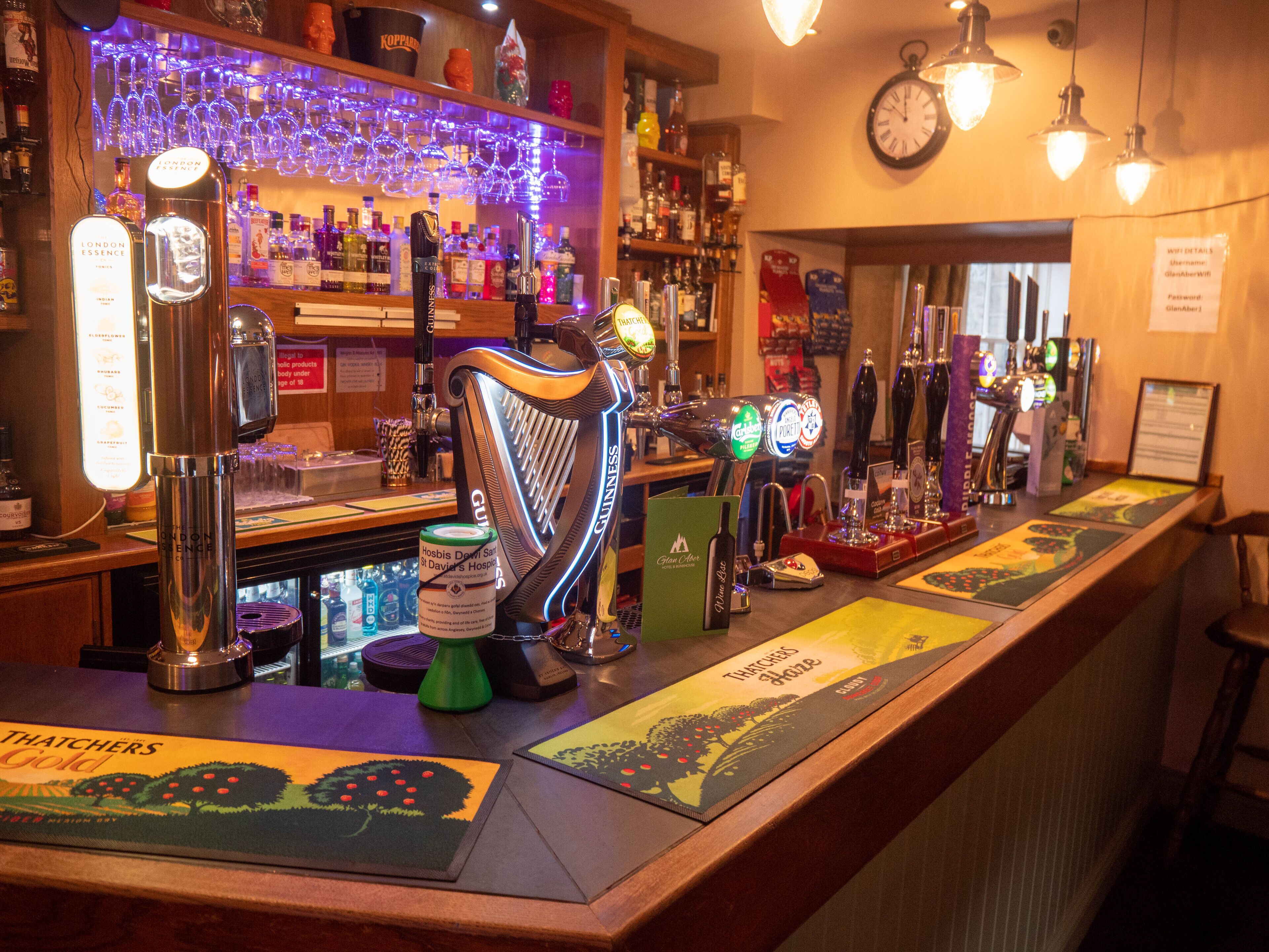 A bar with multiple beer taps, a clock, and a variety of bottles and glasses on shelves.