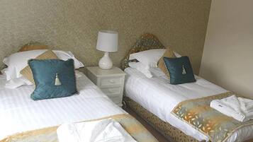 Two single beds with white linens, blue pillows, and a white bedside table with a lamp.