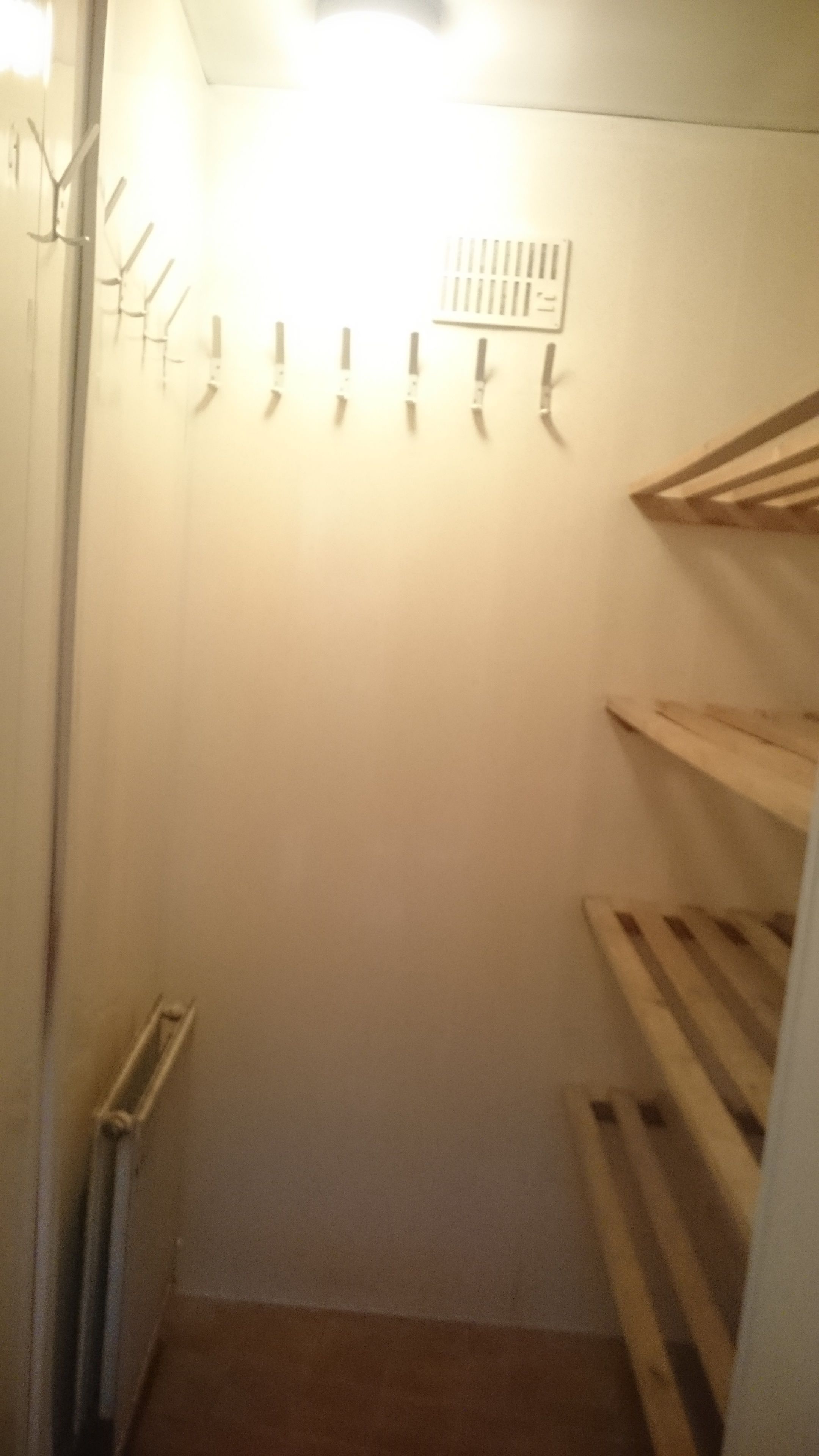 A narrow walk-in closet with a radiator on the left, a light fixture above, and wooden shelves on the right.