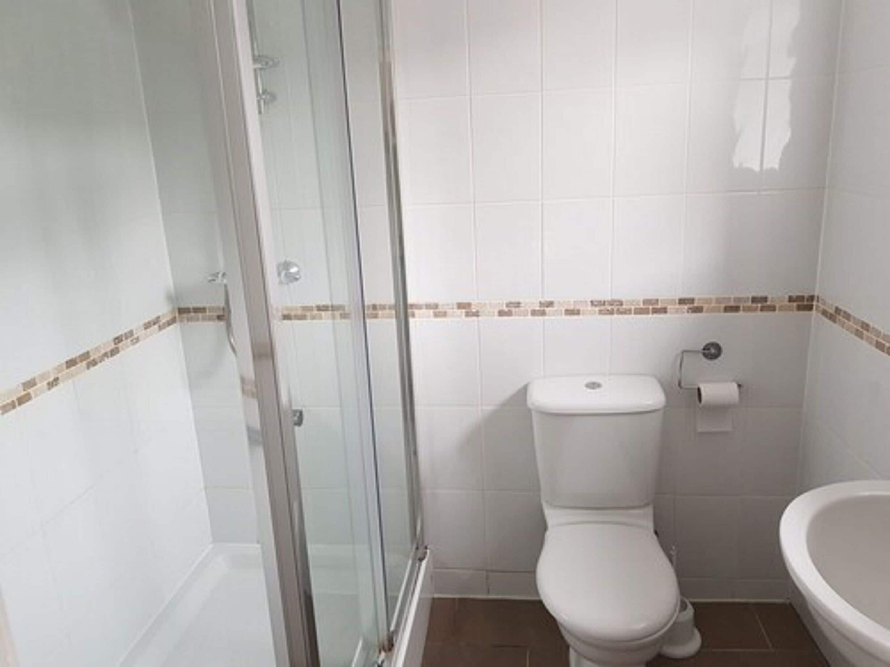 A bathroom with a glass shower enclosure, a toilet, and a sink.