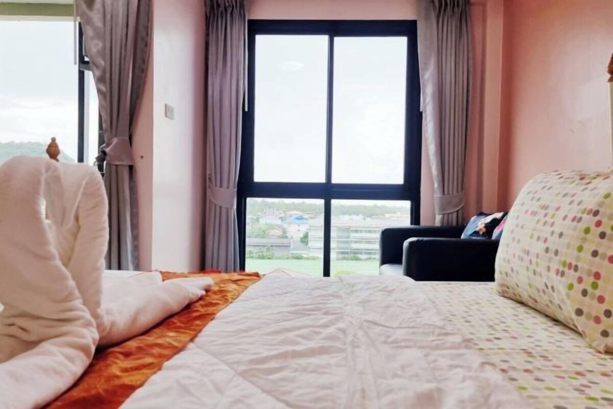 A hotel room with a large window, a bed with a patterned bedspread, a sofa, and curtains.