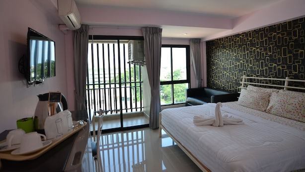 A hotel room with a bed, a TV, a desk with a coffee maker, and a window with a view of greenery. - Kwanchanok Ville (Hua Hin)