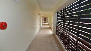 A corridor with a tiled floor, a red fire alarm on the left, and a black metal fence on the right. - Kwanchanok Ville (Hua Hin)