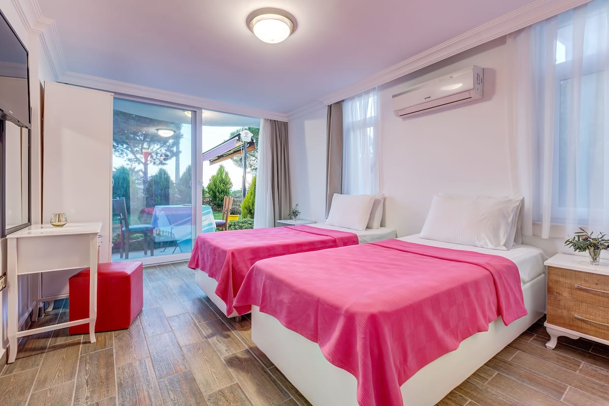A hotel room with two beds, a desk, and a sliding glass door leading to an outdoor area.
