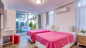 Habitación de hotel con dos camas, un escritorio y ventana con vista a un jardín.