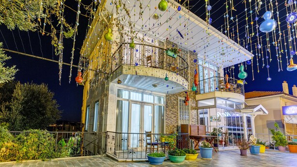 Un edificio de dos pisos con balcón, ventanas grandes y adornos colgantes.