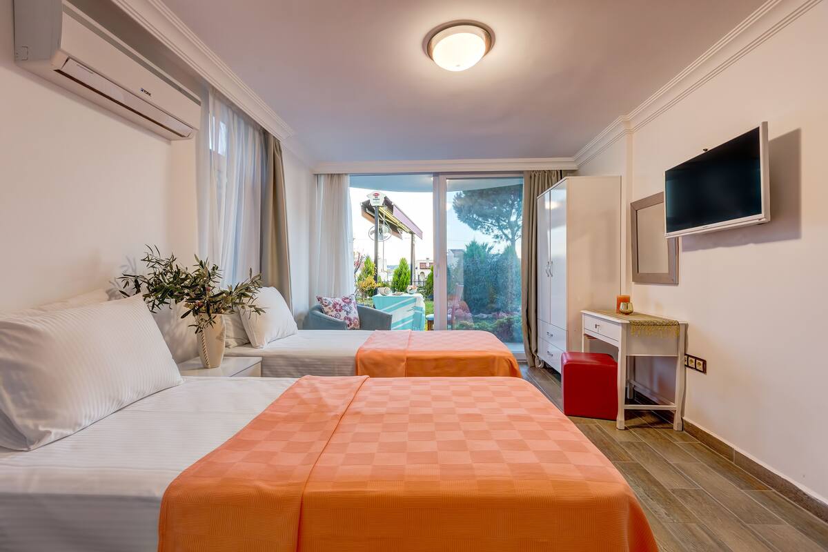 A hotel room with two beds, a desk, a TV, and a view of the outdoors.