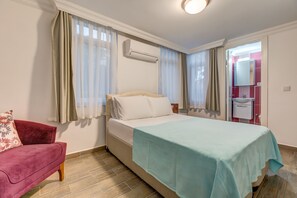 Un dormitorio con cama, un sofá rojo y un baño visible a través de una puerta abierta.