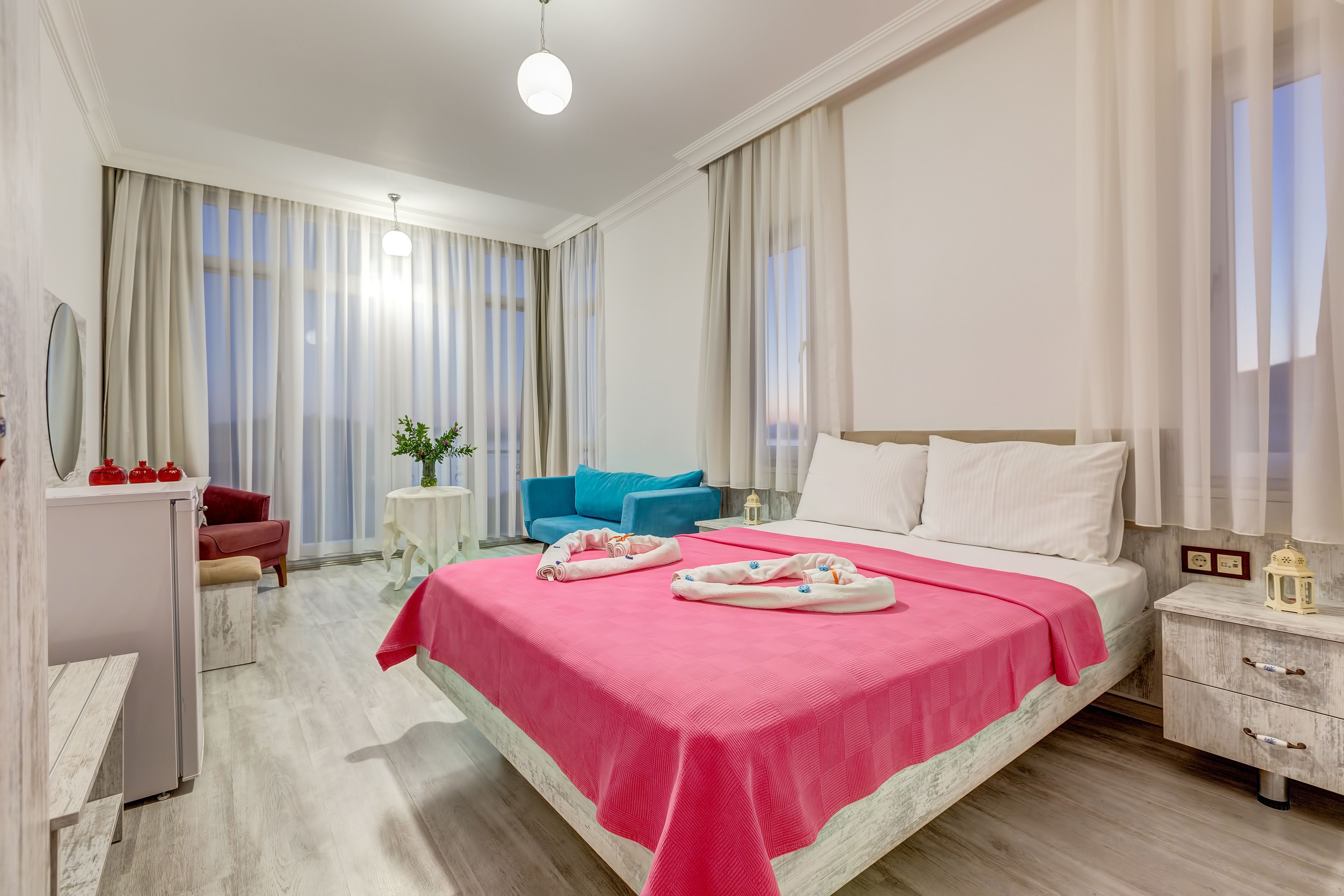 Ein modernes Hotelzimmer mit einem großen Bett, einem Schreibtisch, einem Stuhl und einem kleinen Tisch mit einer Pflanze.