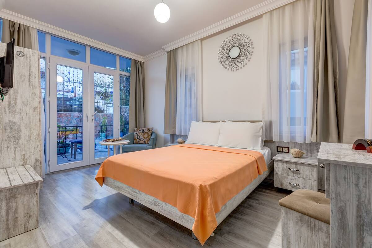 A bedroom with a bed, a nightstand, a desk, and a view of the outside.