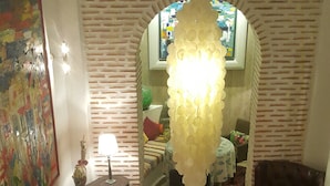 Un accogliente soggiorno con un divano viola, un tavolino in vetro con fiori, un lampadario e un muro in mattoni.