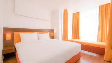 Habitación de hotel con cama, mesita de noche, lámpara de pared y ventana con cortinas.