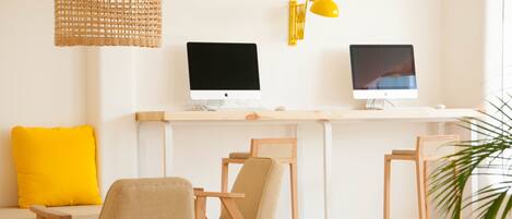 A workspace with two Apple iMac computers, a yellow lamp, and a woven pendant light.