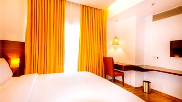 Habitación de hotel con una cama grande, un escritorio con una silla, un televisor en la pared y una ventana con cortinas.